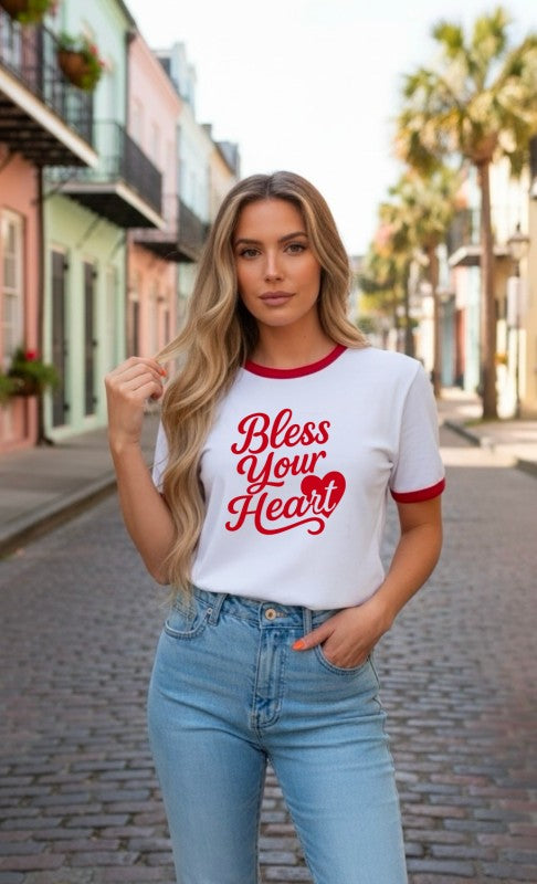 Model wearing a white ringer t-shirt with red trim and red ‘Bless Your Heart’ graphic text, paired with light wash jeans.