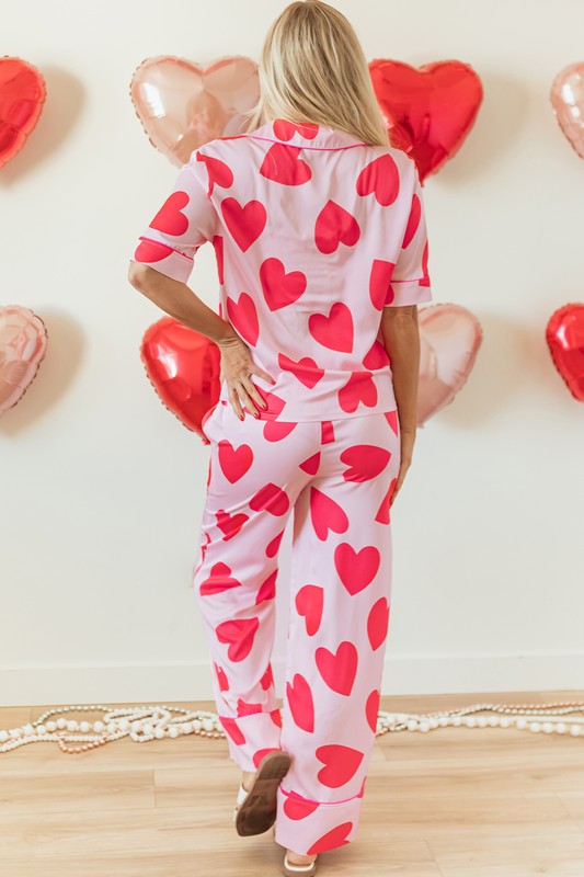 Person wearing heart-patterned pajamas with heart-shaped balloons in the background.